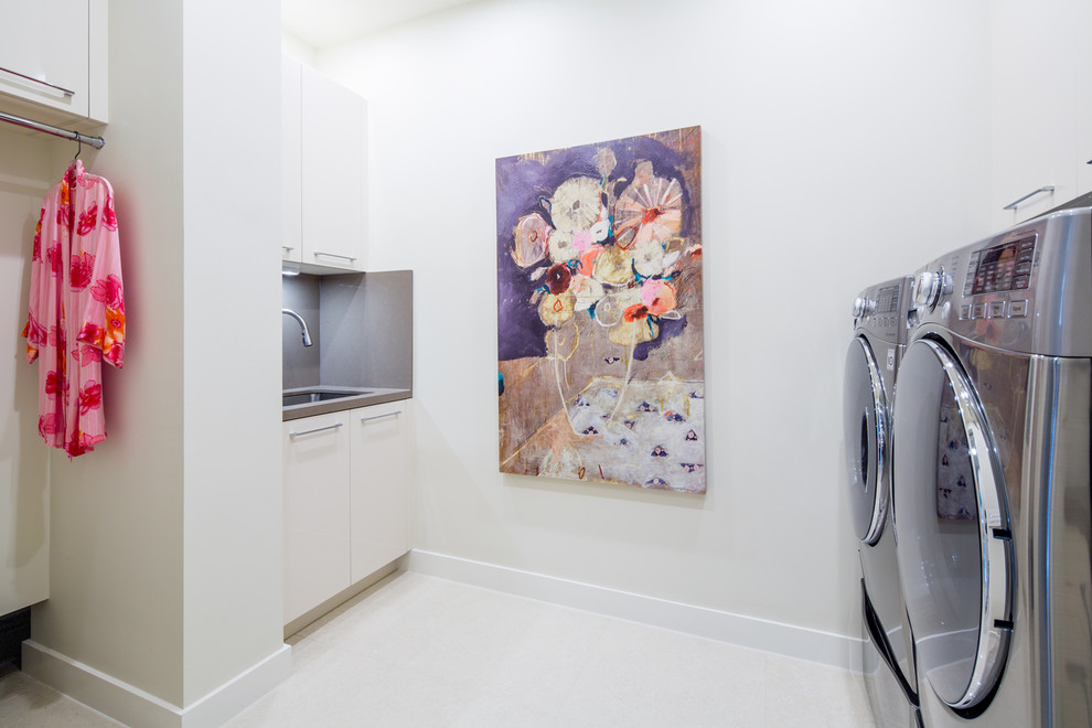 Idéer för stora funkis tvättstugor enbart för tvätt, med en enkel diskho, släta luckor, vita skåp, bänkskiva i kvarts, beige väggar, klinkergolv i porslin och en tvättmaskin och torktumlare bredvid varandra