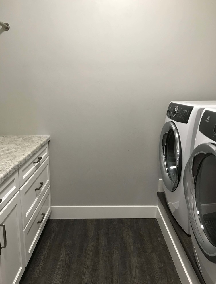 Immagine di una piccola sala lavanderia con ante in stile shaker, ante bianche, top in laminato, pareti grigie, pavimento in vinile, lavatrice e asciugatrice affiancate e pavimento marrone