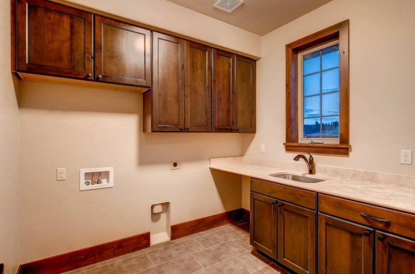 Klassischer Hauswirtschaftsraum in L-Form mit Unterbauwaschbecken, Schrankfronten mit vertiefter Füllung, dunklen Holzschränken, beiger Wandfarbe und Waschmaschine und Trockner nebeneinander in Denver