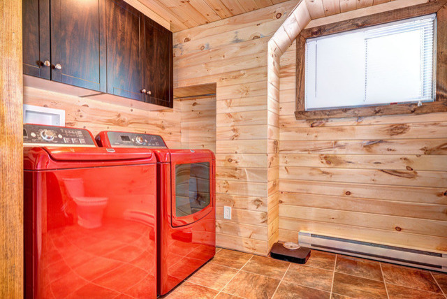 Ejemplo de cuarto de lavado rural pequeño con puertas de armario de madera en tonos medios, paredes marrones, suelo de baldosas de porcelana y lavadora y secadora juntas