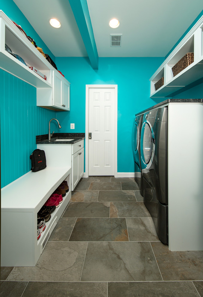 Immagine di una piccola lavanderia multiuso rustica con lavello sottopiano, ante con riquadro incassato, ante bianche, top in granito, pareti blu, pavimento in ardesia e lavatrice e asciugatrice affiancate