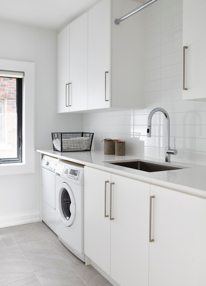 Foto på en mellanstor funkis vita tvättstuga enbart för tvätt, med en undermonterad diskho, släta luckor, vita skåp, vita väggar och en tvättmaskin och torktumlare bredvid varandra