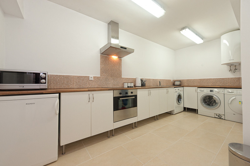 Large minimalist l-shaped porcelain tile utility room photo in Malaga with flat-panel cabinets, white cabinets, wood countertops and white walls