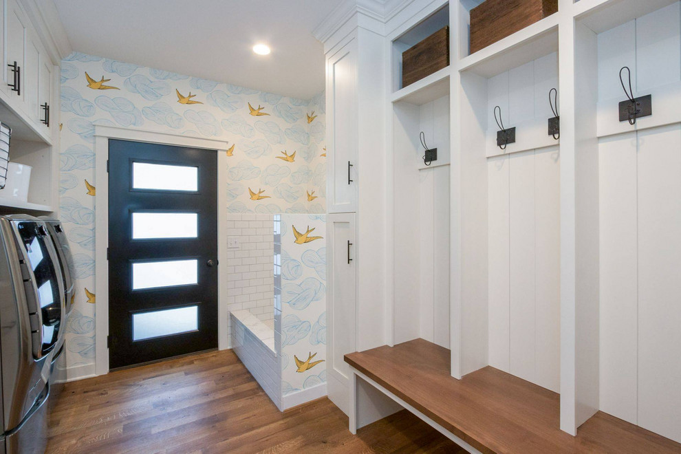 Exempel på en stor lantlig parallell tvättstuga, med en allbänk, skåp i shakerstil, vita skåp, flerfärgade väggar, mellanmörkt trägolv, en tvättmaskin och torktumlare bredvid varandra och brunt golv
