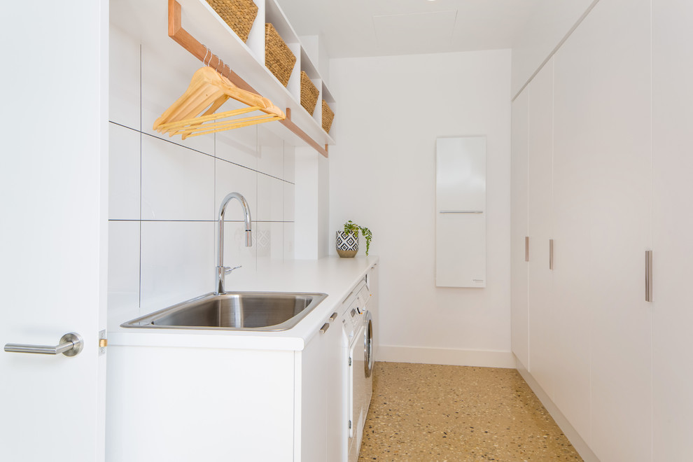 Diseño de lavadero multiusos y de galera minimalista con paredes blancas, suelo de cemento, lavadora y secadora juntas y fregadero encastrado