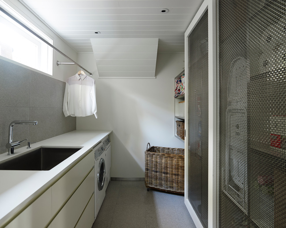 Foto di una lavanderia design con lavello sottopiano, ante lisce, ante bianche, pareti bianche e lavatrice e asciugatrice affiancate