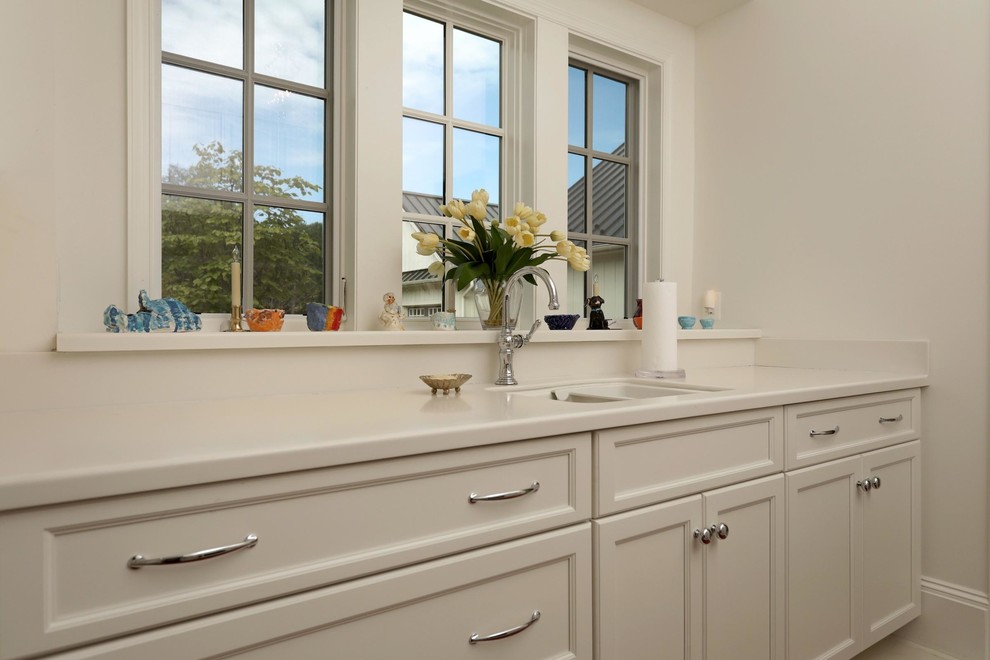 Klassisk inredning av en mellanstor parallell tvättstuga enbart för tvätt, med en dubbel diskho, vita skåp, vita väggar, en tvättmaskin och torktumlare bredvid varandra och vitt golv