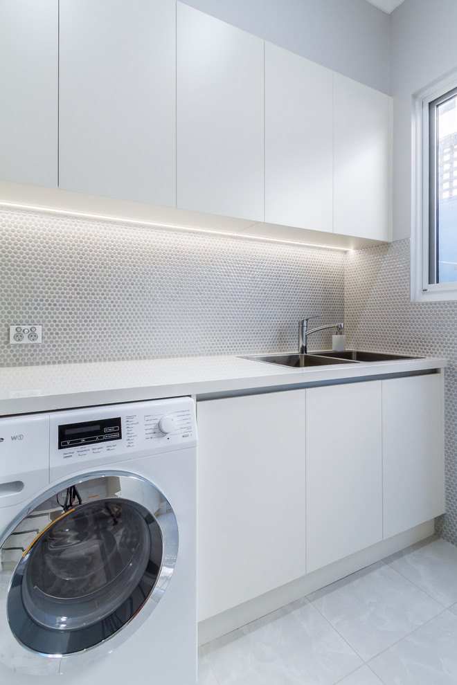 Idéer för att renovera en mellanstor funkis vita linjär vitt tvättstuga enbart för tvätt, med en nedsänkt diskho, släta luckor, vita skåp, bänkskiva i kvarts, grå väggar, klinkergolv i porslin, en tvättmaskin och torktumlare bredvid varandra och grått golv