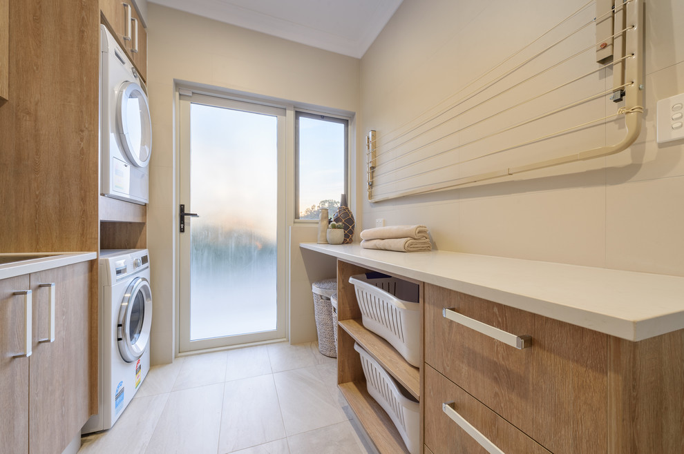 Large traditional galley separated utility room in Perth with a single-bowl sink, flat-panel cabinets, medium wood cabinets, engineered stone countertops, beige walls, porcelain flooring, a stacked washer and dryer and beige floors.