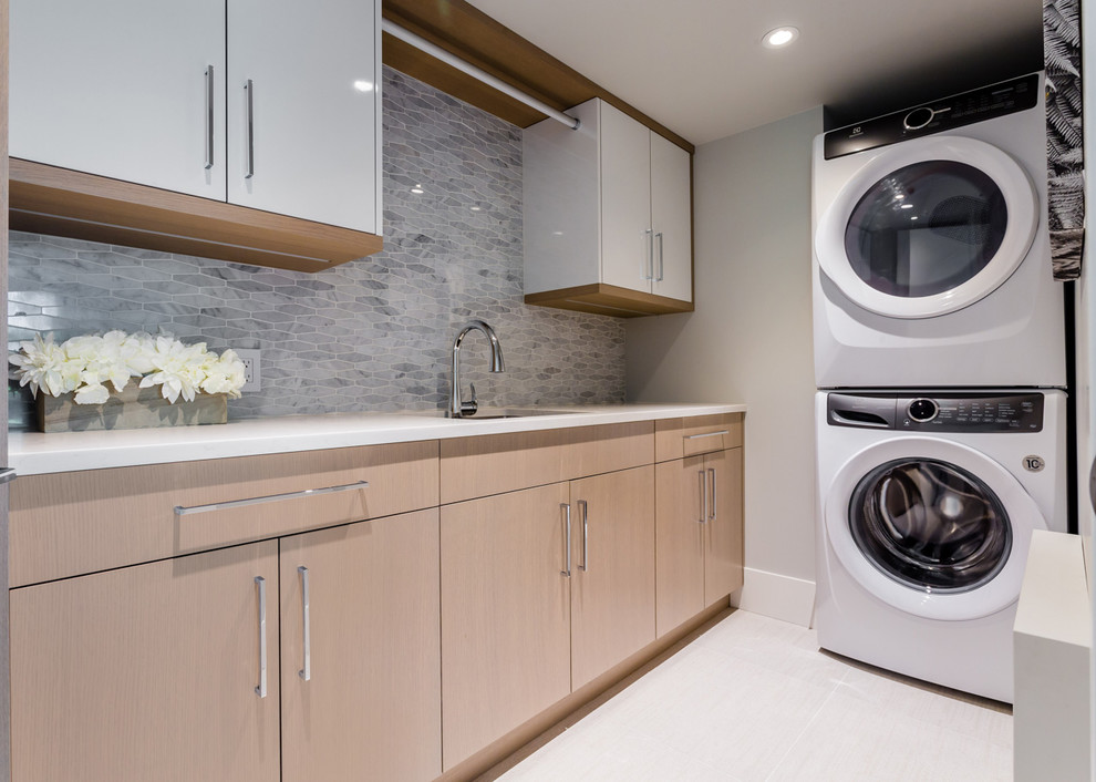 This is an example of a medium sized modern utility room in Vancouver with a submerged sink, flat-panel cabinets, light wood cabinets, grey walls, porcelain flooring, a stacked washer and dryer, white floors and white worktops.
