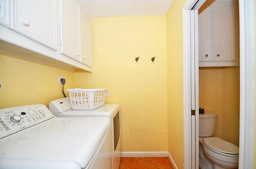 Immagine di una piccola sala lavanderia classica con ante con bugna sagomata, ante bianche, pareti gialle, pavimento con piastrelle in ceramica e lavatrice e asciugatrice affiancate