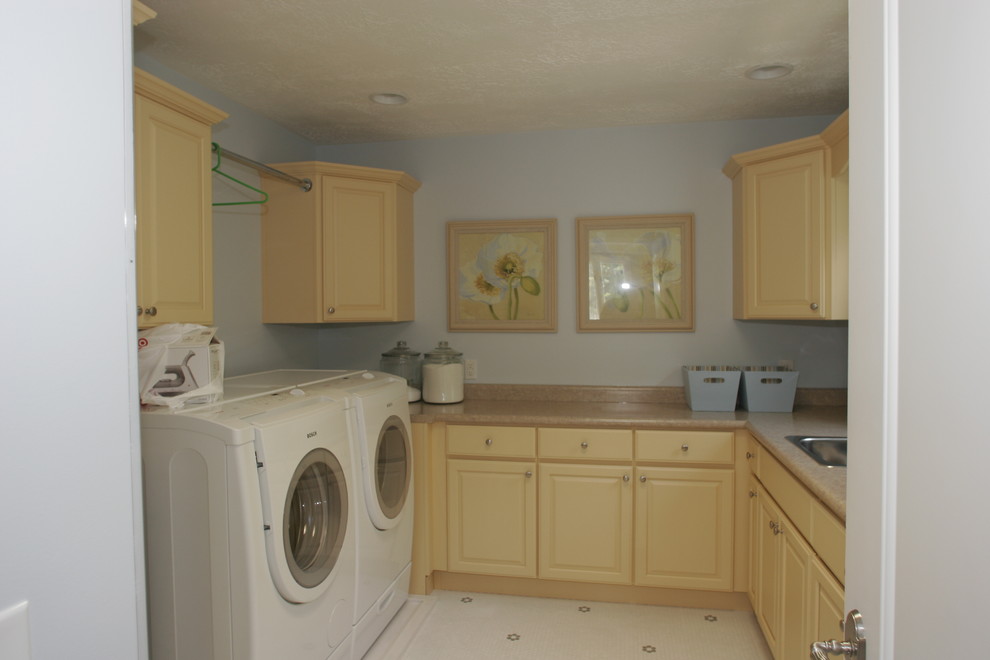 Esempio di una sala lavanderia tradizionale di medie dimensioni con lavello da incasso, ante con bugna sagomata, ante gialle, top in superficie solida, pareti blu, pavimento con piastrelle in ceramica e lavatrice e asciugatrice affiancate
