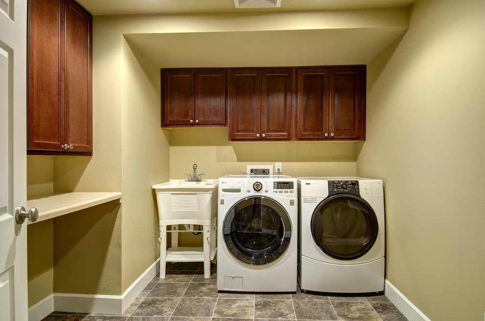 Idee per una sala lavanderia classica di medie dimensioni con lavatoio, ante con bugna sagomata, ante in legno bruno, top in superficie solida, pareti gialle, pavimento in ardesia, lavatrice e asciugatrice affiancate, pavimento marrone e top beige