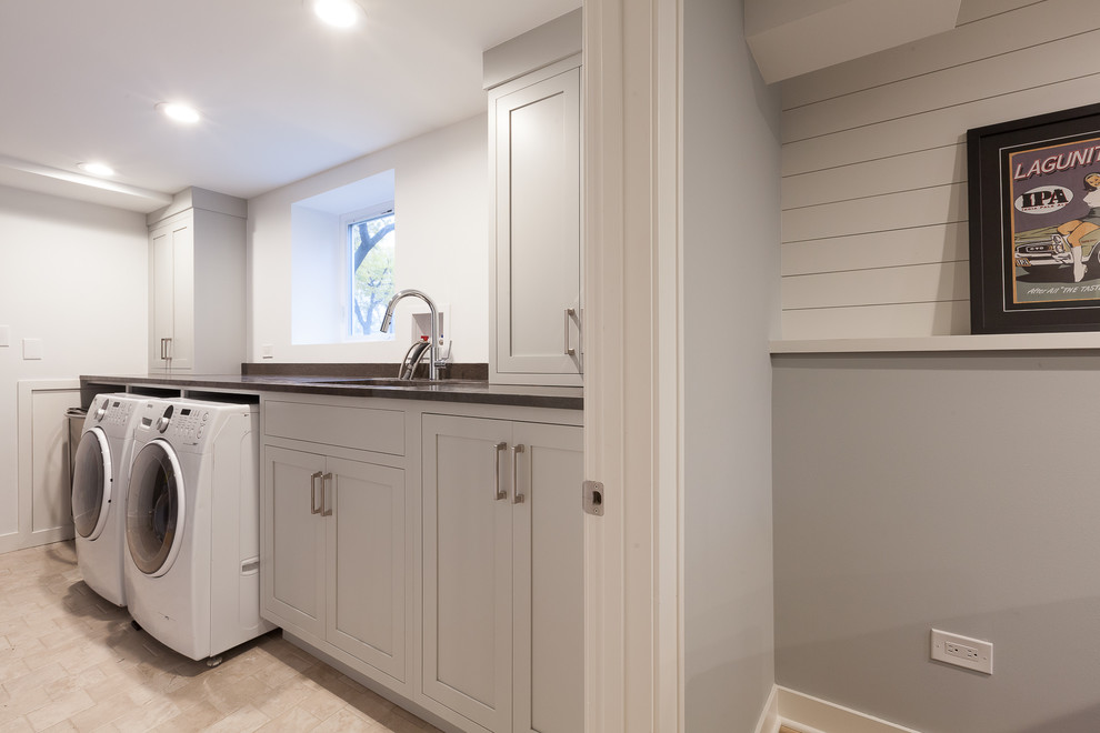 Example of a mid-sized transitional single-wall ceramic tile and beige floor utility room design in Chicago with an undermount sink, flat-panel cabinets, gray cabinets, granite countertops, gray walls, a side-by-side washer/dryer and black countertops