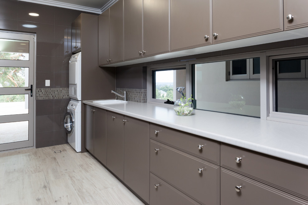 Modern single-wall utility room in Perth with laminate countertops, a stacked washer and dryer, raised-panel cabinets, white worktops and brown cabinets.