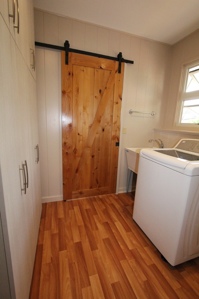 Immagine di una lavanderia multiuso tradizionale di medie dimensioni con lavatoio, pareti bianche, pavimento in legno massello medio e lavatrice e asciugatrice affiancate