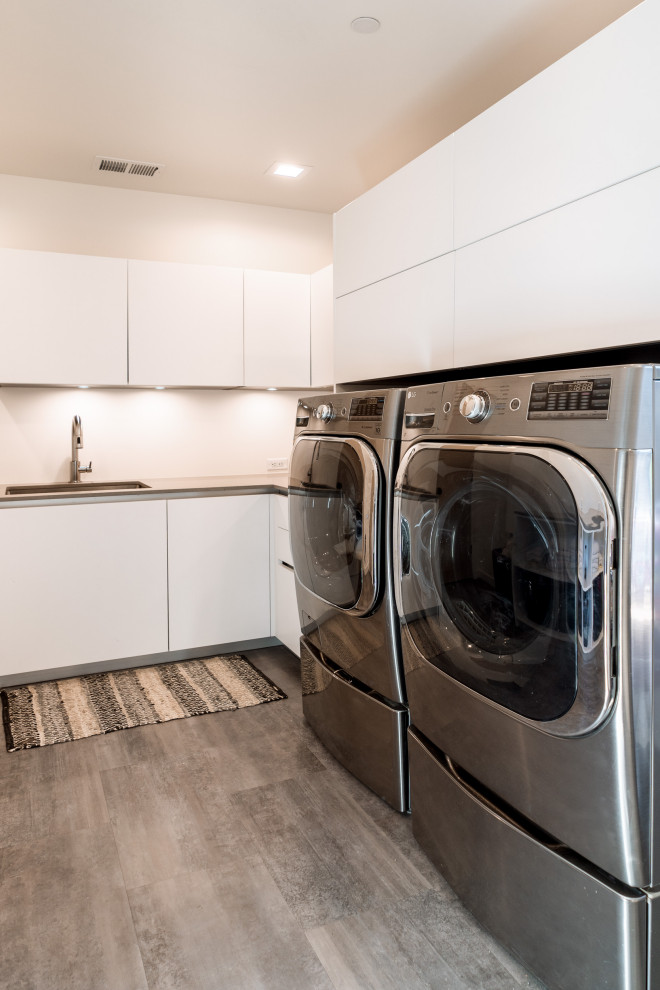 Idéer för en mellanstor modern grå l-formad tvättstuga enbart för tvätt, med en undermonterad diskho, släta luckor, vita skåp, bänkskiva i kvarts, vita väggar, klinkergolv i porslin, en tvättmaskin och torktumlare bredvid varandra och grått golv