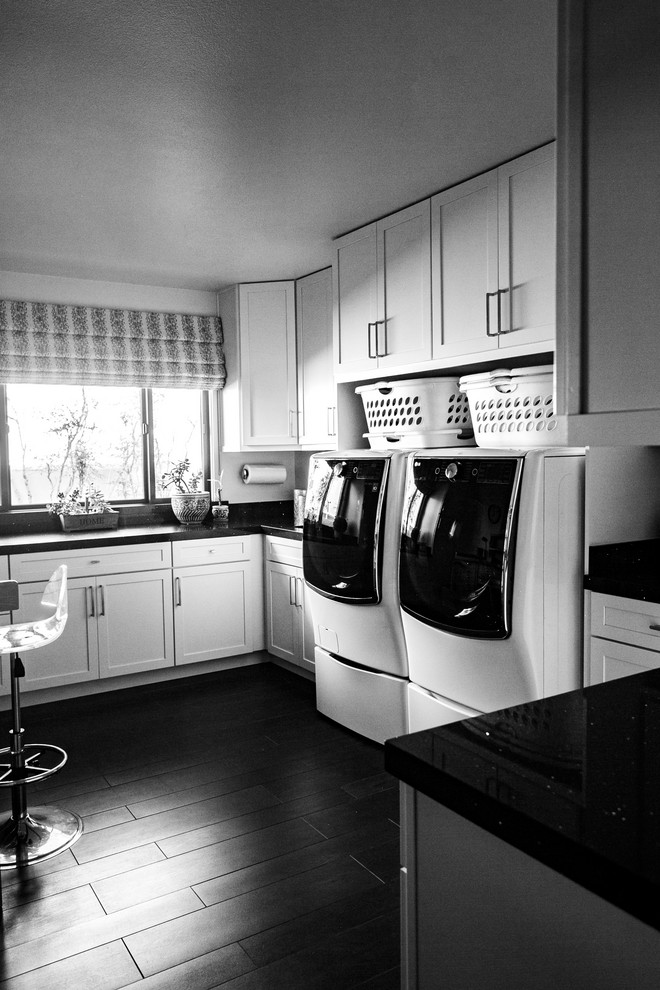 This is an example of a contemporary separated utility room in San Diego with ceramic flooring, a side by side washer and dryer, black floors, black worktops and white cabinets.