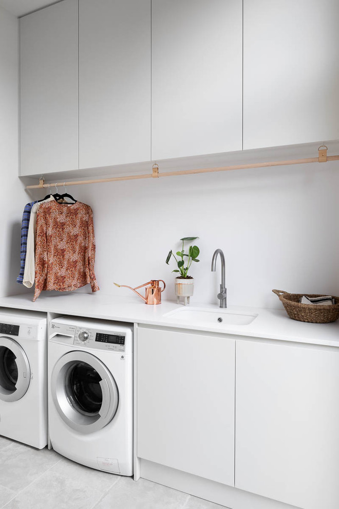 Einzeilige, Mittelgroße Moderne Waschküche mit Waschmaschine und Trockner nebeneinander, Unterbauwaschbecken, flächenbündigen Schrankfronten, grauen Schränken, grauem Boden und weißer Arbeitsplatte in Melbourne