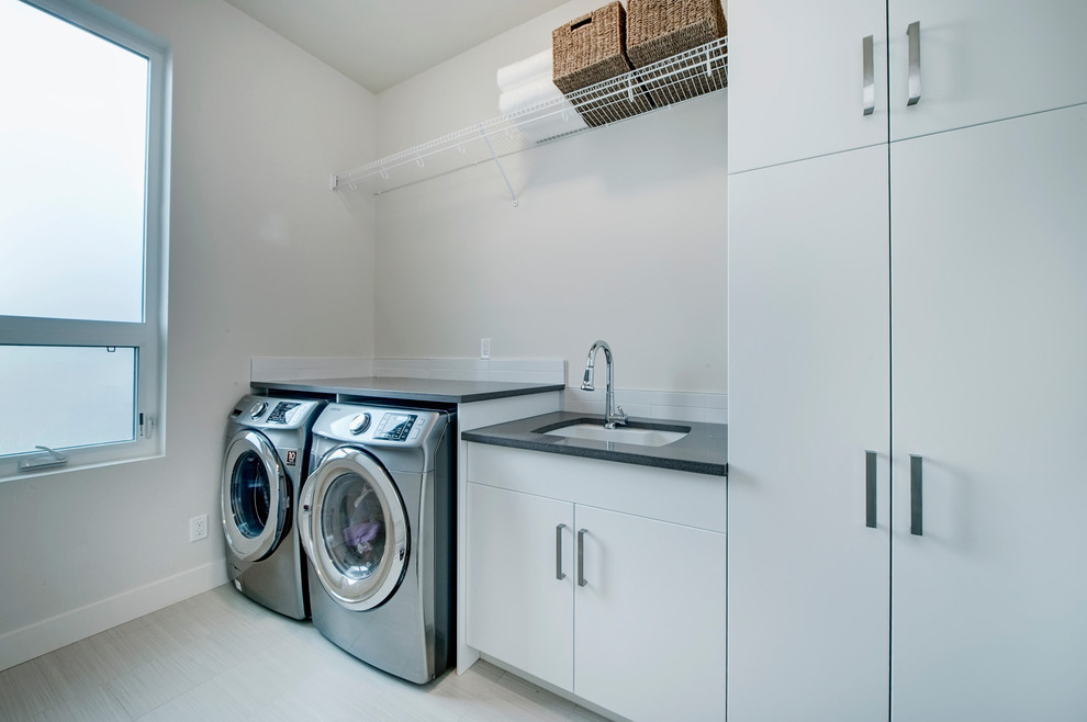 Idéer för att renovera en mellanstor funkis linjär tvättstuga enbart för tvätt, med en undermonterad diskho, släta luckor, vita skåp, bänkskiva i kvarts, vita väggar, klinkergolv i keramik och en tvättmaskin och torktumlare bredvid varandra