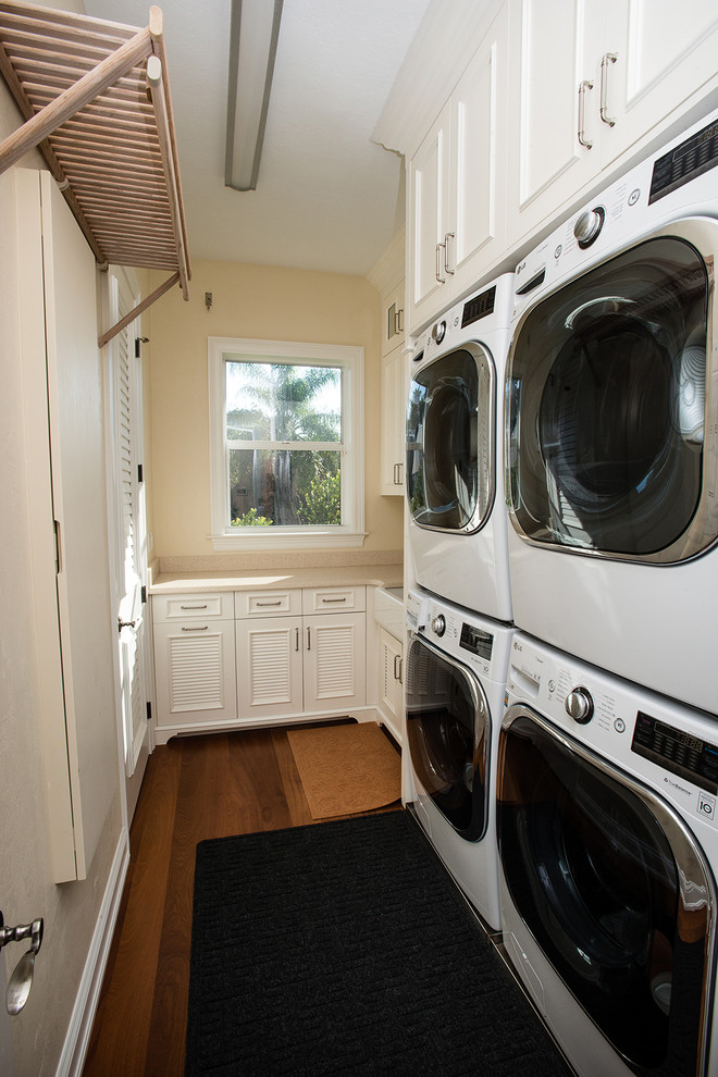 Example of a mid-sized beach style single-wall utility room design in Miami with an undermount sink, shaker cabinets, white cabinets, beige walls and a stacked washer/dryer