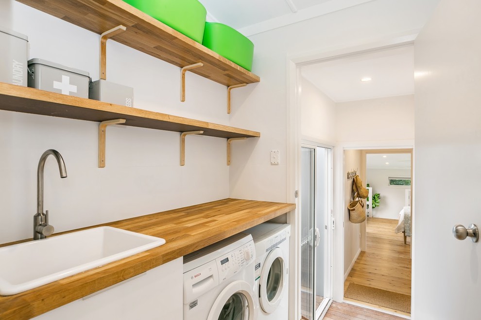 Design ideas for a coastal single-wall separated utility room in Central Coast with a built-in sink, flat-panel cabinets, white cabinets, wood worktops, white walls, medium hardwood flooring, a side by side washer and dryer, brown floors and brown worktops.