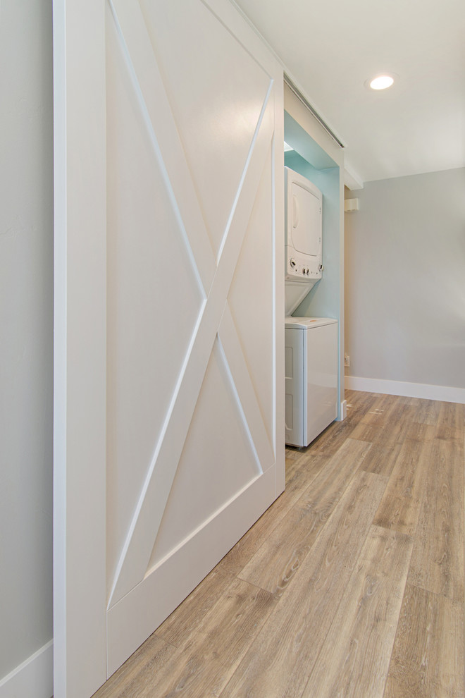 Medium sized nautical single-wall laundry cupboard in San Diego with shaker cabinets, light wood cabinets, quartz worktops, green walls, vinyl flooring, a stacked washer and dryer, grey floors and green worktops.