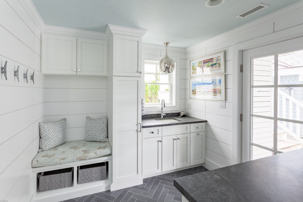 Photo of a large beach style l-shaped utility room in Philadelphia with a submerged sink, flat-panel cabinets, white cabinets, quartz worktops, white walls, porcelain flooring, a side by side washer and dryer, grey floors and grey worktops.