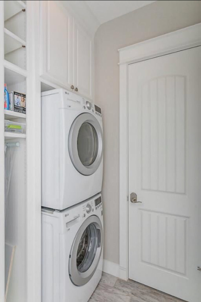 Inspiration for a medium sized beach style single-wall separated utility room in Austin with raised-panel cabinets, white cabinets, grey walls, light hardwood flooring, a stacked washer and dryer and grey floors.