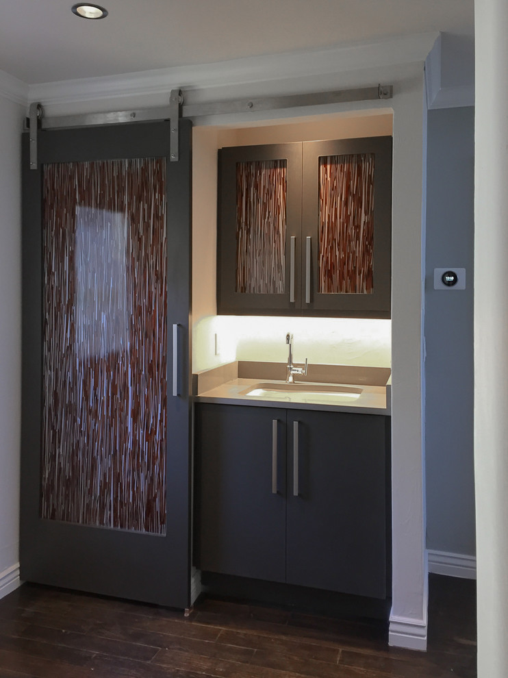 Modern inredning av en mellanstor linjär liten tvättstuga, med en undermonterad diskho, grå väggar, mörkt trägolv, en tvättpelare och brunt golv