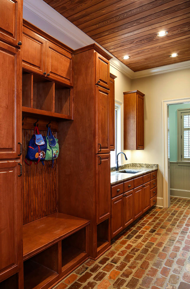 Foto di una grande lavanderia multiuso tradizionale con lavello sottopiano, ante in legno scuro, top in granito, pareti beige, pavimento in mattoni e lavatrice e asciugatrice affiancate