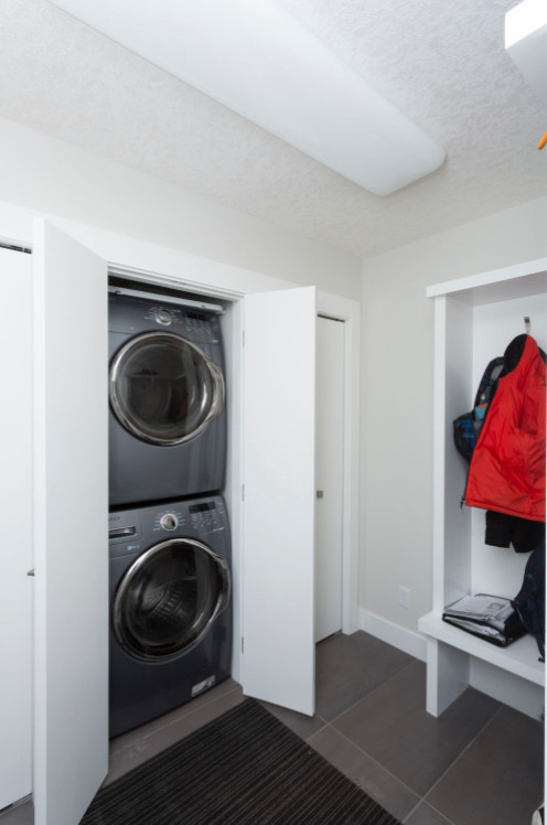 Einzeiliger, Kleiner Moderner Hauswirtschaftsraum mit Waschmaschinenschrank, beiger Wandfarbe, Porzellan-Bodenfliesen, Waschmaschine und Trockner gestapelt und grünem Boden in Calgary
