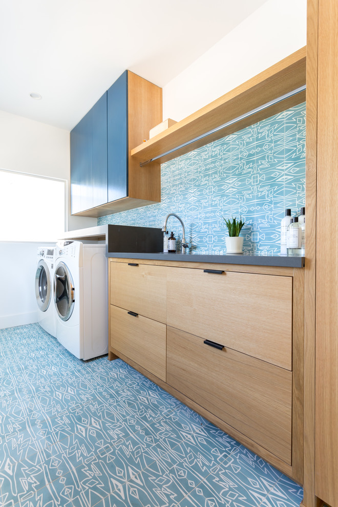 Exempel på en stor modern grå linjär grått tvättstuga enbart för tvätt, med en undermonterad diskho, släta luckor, bänkskiva i kvarts, blå väggar, en tvättmaskin och torktumlare bredvid varandra, skåp i mellenmörkt trä och blått golv