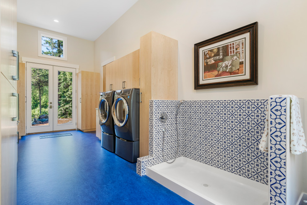 Modelo de lavadero multiusos y lineal contemporáneo con armarios con paneles lisos, puertas de armario de madera clara, paredes blancas, lavadora y secadora apiladas y suelo azul