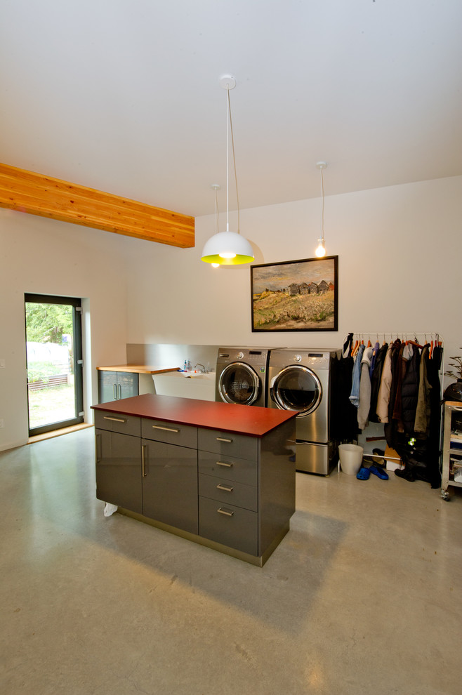 This is an example of an expansive single-wall utility room in Vancouver with an utility sink, flat-panel cabinets, grey cabinets, wood worktops, white walls, concrete flooring and a side by side washer and dryer.