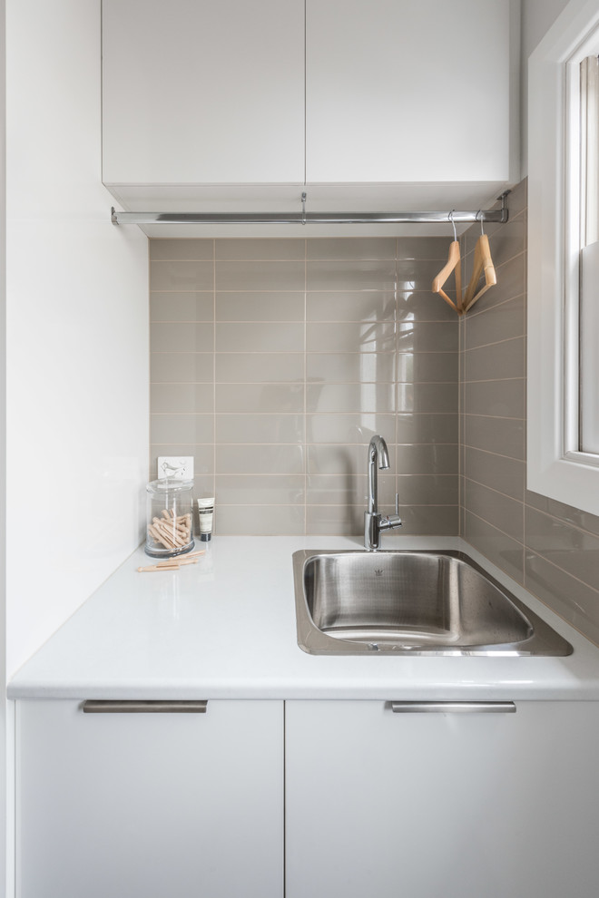 Small trendy medium tone wood floor dedicated laundry room photo in Melbourne with a single-bowl sink, flat-panel cabinets, white cabinets, laminate countertops, gray walls and a stacked washer/dryer