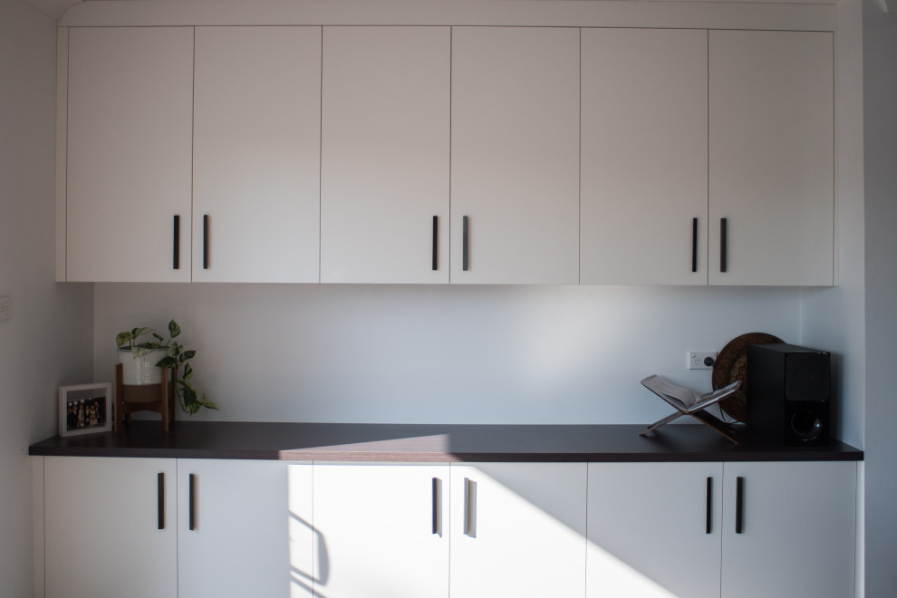 This is an example of a large galley separated utility room in Sydney with a built-in sink, flat-panel cabinets, white cabinets, composite countertops, white walls, a concealed washer and dryer and white worktops.