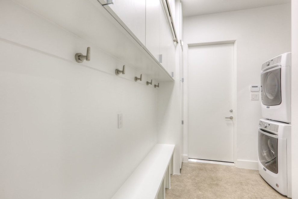 Réalisation d'une buanderie parallèle minimaliste dédiée et de taille moyenne avec un placard à porte plane, des portes de placard blanches, un mur blanc, sol en béton ciré, des machines superposées et un sol beige.