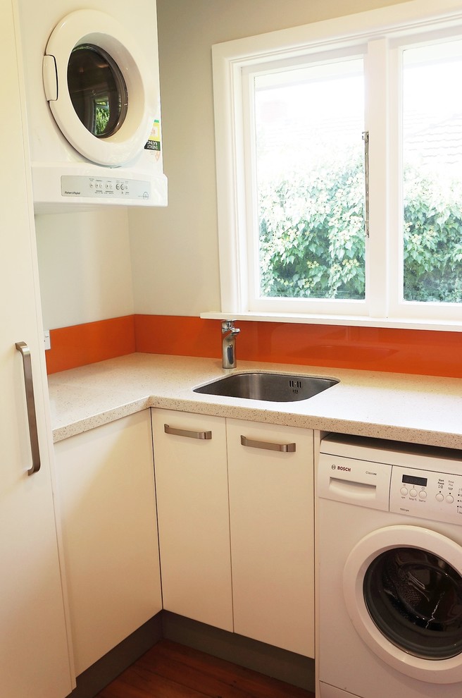 Example of a small trendy l-shaped medium tone wood floor dedicated laundry room design in Christchurch with an undermount sink, quartz countertops and white walls