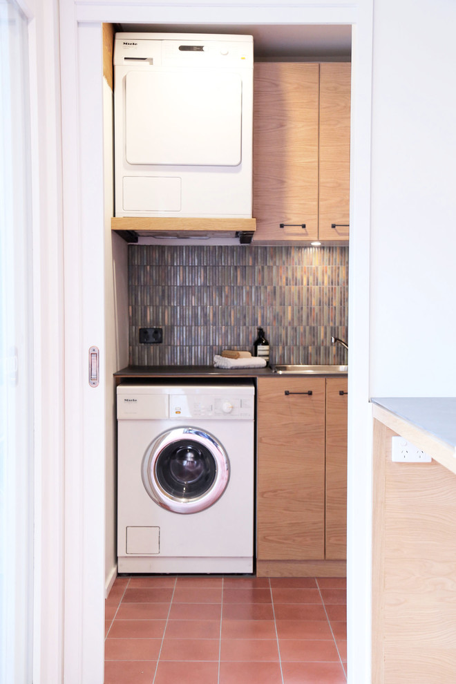 This is an example of a small modern u-shaped separated utility room in Melbourne with flat-panel cabinets, composite countertops, multi-coloured walls, porcelain flooring, a stacked washer and dryer and medium wood cabinets.