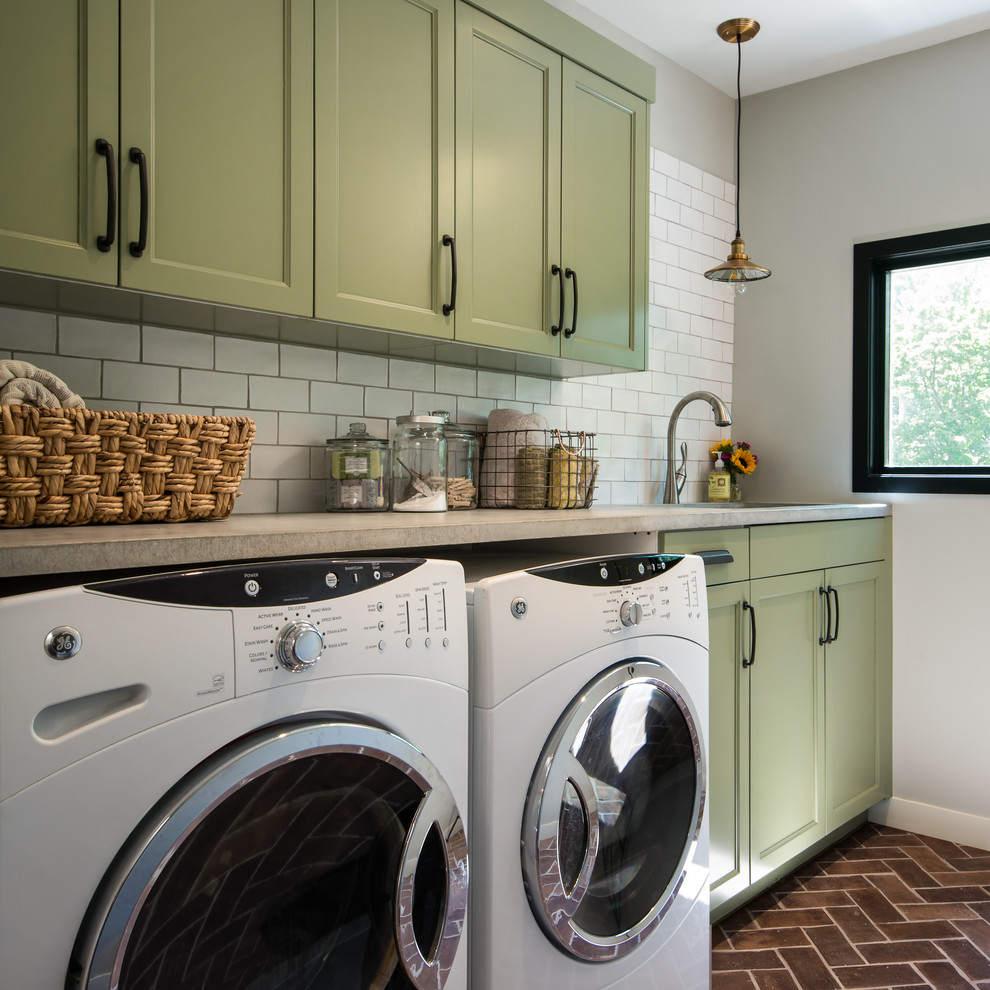 デトロイトにある高級な中くらいなトランジショナルスタイルのおしゃれな洗濯室 (I型、アンダーカウンターシンク、落し込みパネル扉のキャビネット、緑のキャビネット、コンクリートカウンター、グレーの壁、レンガの床、左右配置の洗濯機・乾燥機) の写真