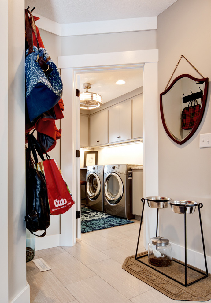 Modelo de cuarto de lavado clásico renovado de tamaño medio con armarios con paneles lisos, paredes blancas, suelo de baldosas de cerámica y lavadora y secadora juntas