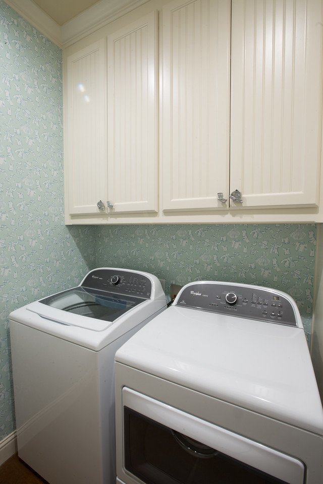 Modelo de armario lavadero lineal clásico pequeño con armarios con paneles empotrados, puertas de armario blancas, paredes azules y lavadora y secadora juntas