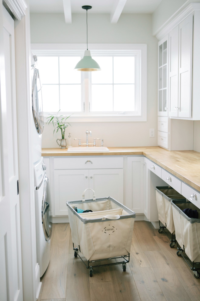 Inspiration for a timeless u-shaped dedicated laundry room remodel in Boston with a drop-in sink, shaker cabinets, white cabinets, white walls, a stacked washer/dryer and beige countertops