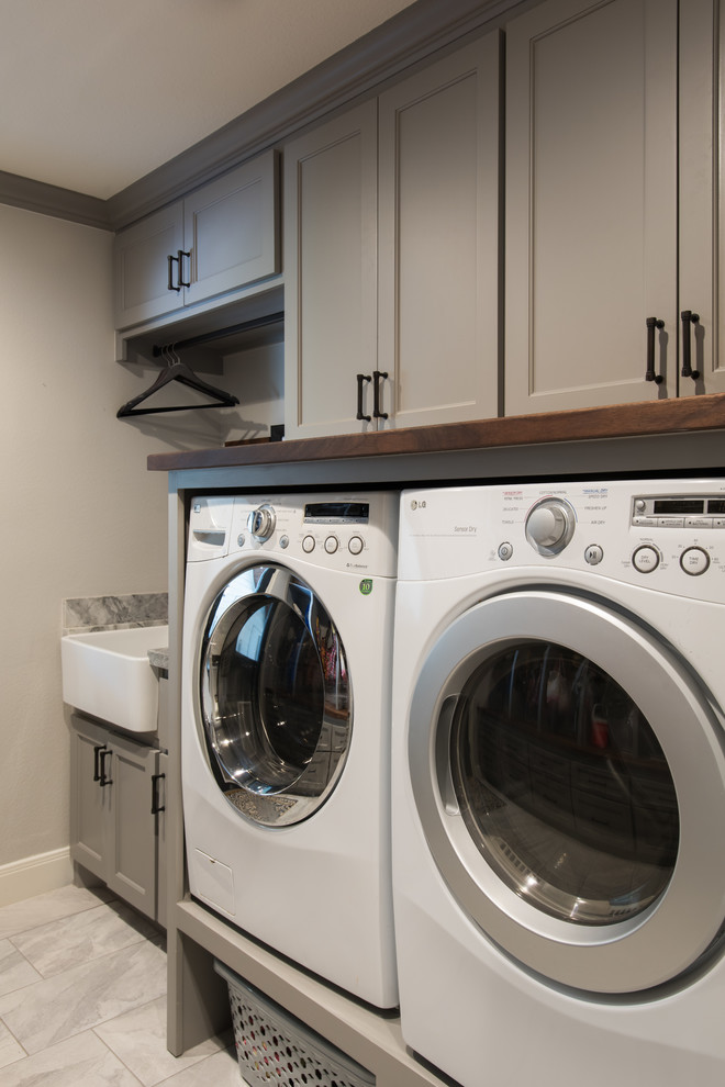 Design ideas for a medium sized traditional galley utility room in Houston with a belfast sink, shaker cabinets, grey cabinets, marble worktops, grey walls, marble flooring and a side by side washer and dryer.