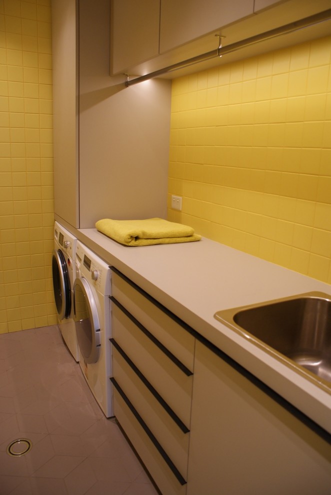 Imagen de cuarto de lavado lineal contemporáneo pequeño con fregadero encastrado, puertas de armario grises, encimera de laminado, paredes amarillas, suelo de baldosas de porcelana y lavadora y secadora juntas