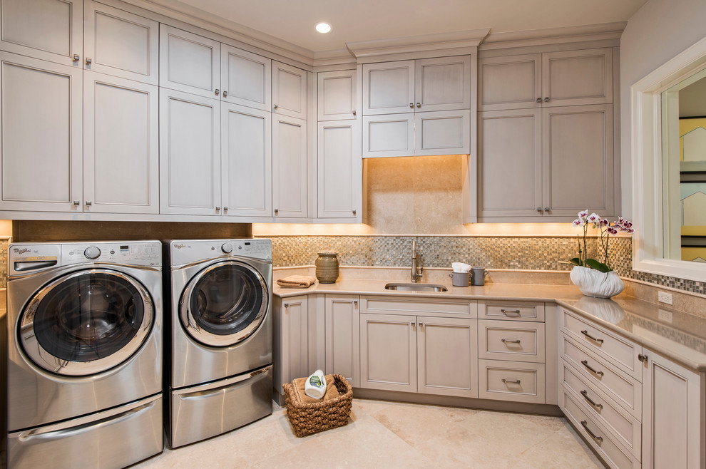 Exempel på en stor klassisk u-formad tvättstuga, med en undermonterad diskho, luckor med upphöjd panel, grå skåp, granitbänkskiva, bruna väggar, travertin golv och en tvättmaskin och torktumlare bredvid varandra