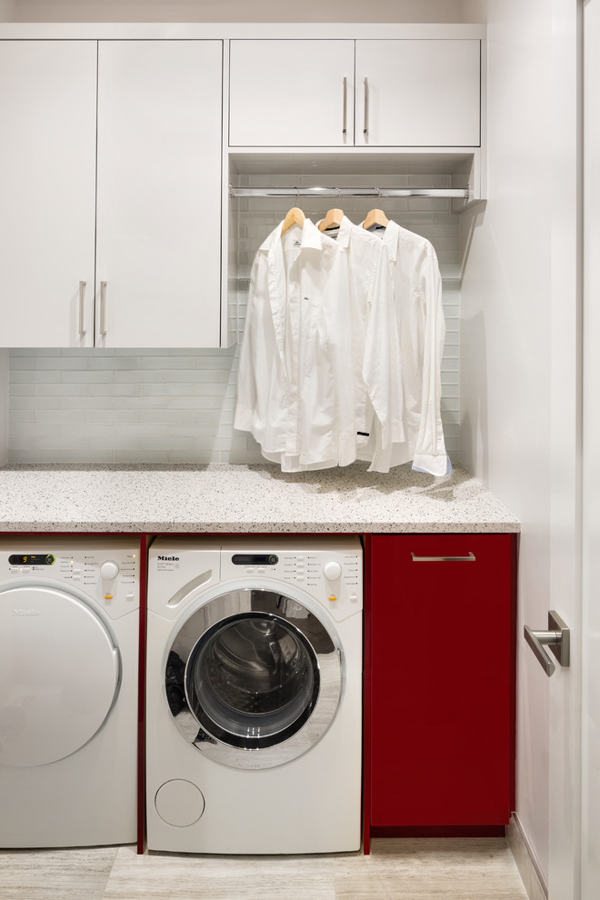 Modelo de lavadero minimalista pequeño con armarios con paneles lisos, puertas de armario rojas, encimera de cuarzo compacto, paredes blancas, suelo de baldosas de porcelana y lavadora y secadora juntas