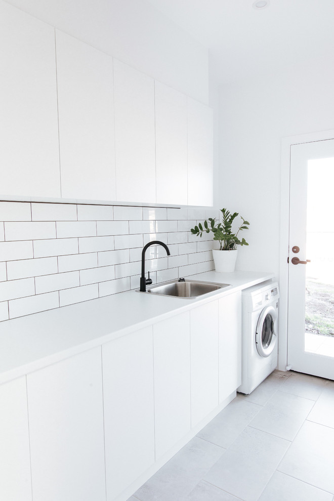 Modern inredning av en mellanstor vita linjär vitt tvättstuga enbart för tvätt, med en nedsänkt diskho, släta luckor, vita skåp, laminatbänkskiva, vita väggar, grått golv och laminatgolv