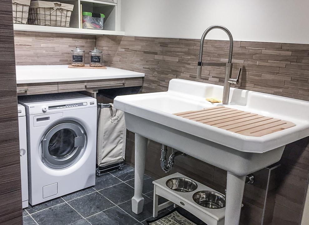 Photo of a medium sized traditional l-shaped utility room in Calgary with an utility sink, flat-panel cabinets, grey cabinets, engineered stone countertops, beige walls, slate flooring and a side by side washer and dryer.